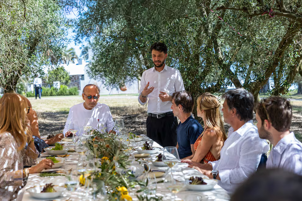 Invitados sentados a la mesa mientras sous chef explica el menú exclusivo pensado para ellos.